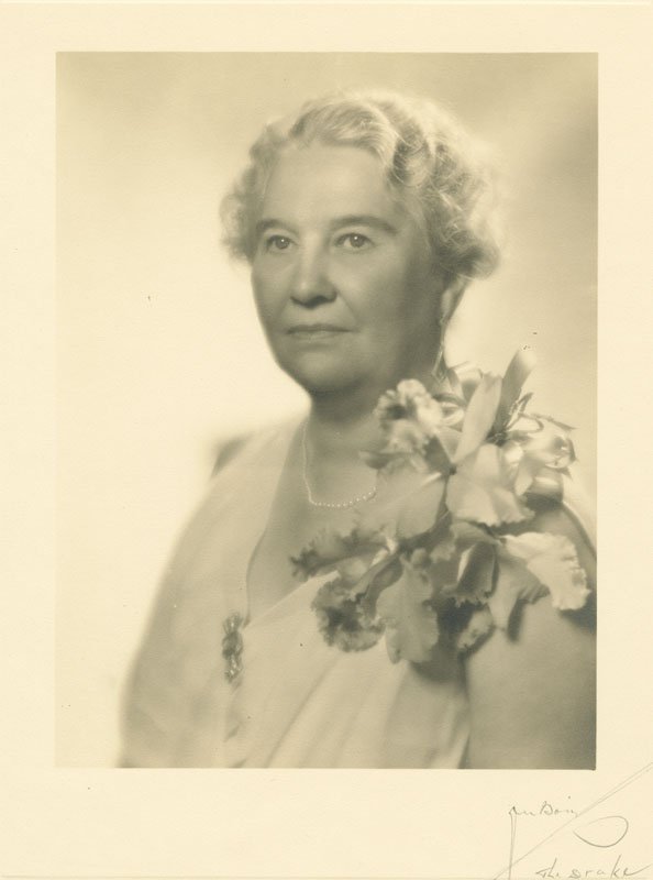 Black-and-white formal photographic portrait of Elizabeth Foss Wilson, circa 1930s. Elizabeth is shown in three-quarters profile in a light-colored dress with a large corsage on her left shoulder. She is an older white woman with short, marcelled hair.