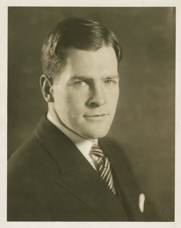 Black-and-white formal photographic portrait of Edward Foss Wilson. Edward is a young white man with short dark hair. He is wearing a dark suit and tie, and is shown from the shoulders up.