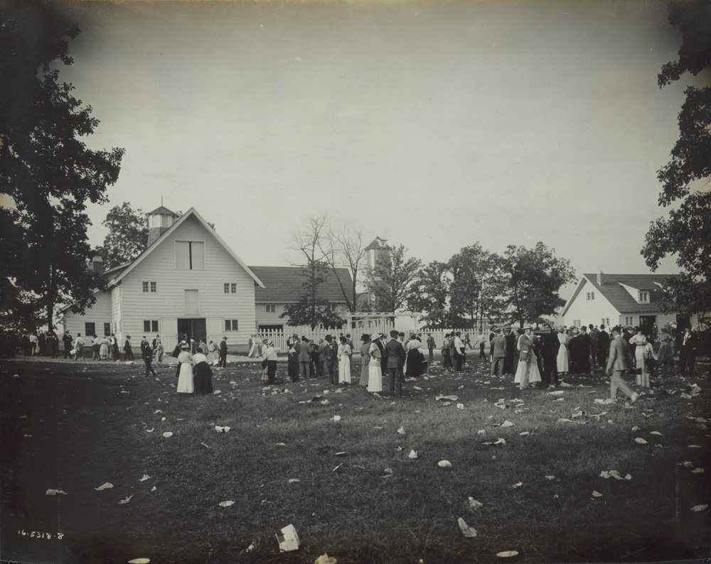 Black-and-white photograph of a Wilson & Co. picnic at Edellyn Farm. A crowd of people standard near farm buildings.