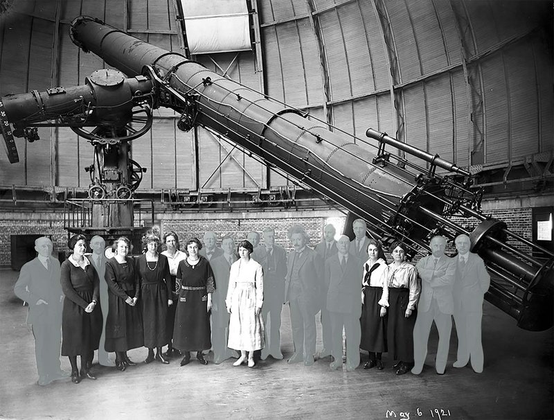 Black and white image of men and women standing in a dome with a very large telescope. The men in the picture are "grayed out" so they are less prominent, and the women in the picture become more foregrounded.